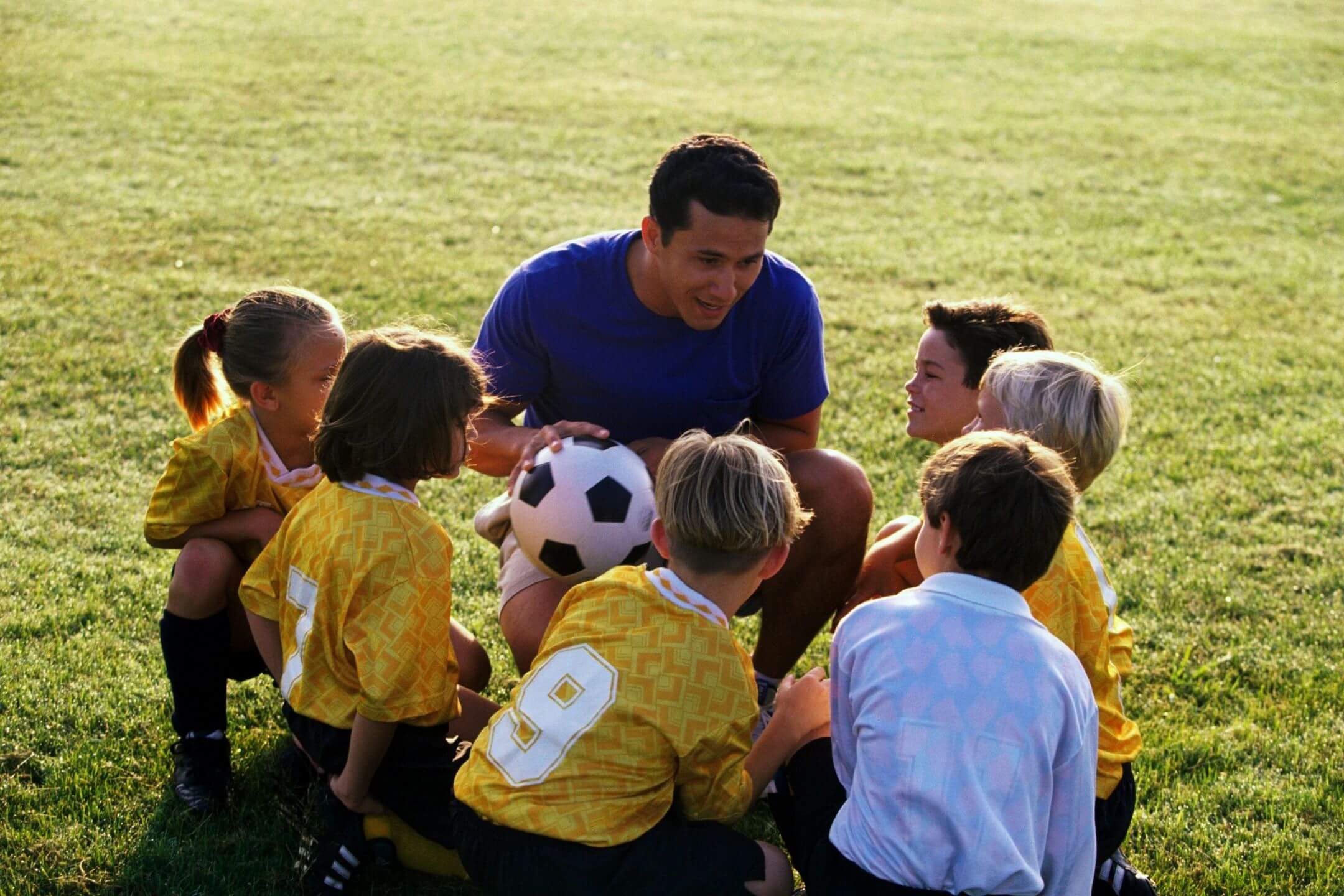 A group of young children sitting around a soccer ball.